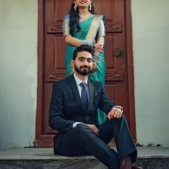 A stylish portrait of a couple, the groom seated while his partner stands behind him, both looking confident and happy.
