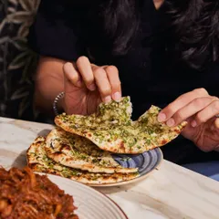 A hand tears into a piece of our Chilli Garlic Naan. It's soft, chewy, and packed with flavour, ideal for scooping up rich curries.