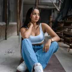 A full-body shot that captures the complete street fashion look, from the casual crop top and denim to the fresh white sneakers. The industrial setting adds a gritty, urban texture to the photo.