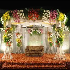 A traditional stage setup for a wedding reception, featuring a colorful explosion of flowers on a raised platform with a classic sofa for seating.