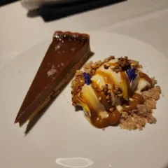 A slice of rich chocolate tart served with vanilla ice cream, caramel sauce, and a crunchy crumble. A dessert for true chocolate lovers.