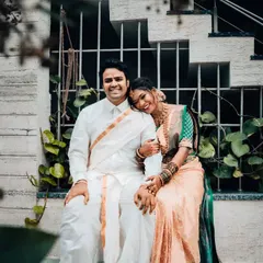 A happy portrait of a newly married couple in traditional South Indian wedding attire. The bride rests her head on her husband's shoulder, a simple gesture full of love.