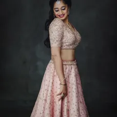 An elegant studio portrait in a soft pink lehenga. The simple, dark background makes the delicate embroidery and the model's happy expression the main focus of the image.