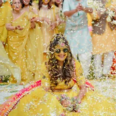 The bride, looking cool and happy in her sunglasses, gets showered with petals during her vibrant Haldi ceremony.