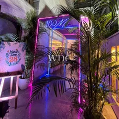 A cool and modern entrance for a birthday party. A neon archway, surrounded by potted palms, creates a fun and inviting welcome for the guests.