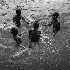 Four friends play together in the water, their joy and camaraderie captured from above in a lively black and white photograph about friendship.