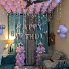 A classic birthday room setup featuring dozens of pink and purple balloons covering the ceiling, complete with silver ribbons.