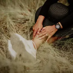 A detail shot focusing on the small things. This artistic photo captures a person's hands and sneakers nestled in tall, dry grass, creating a feeling of being grounded and connected to nature during a photoshoot.