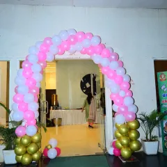 A classic balloon arch at the entrance of a party hall. This pink, white, and gold arch creates a festive and welcoming entry point for guests.