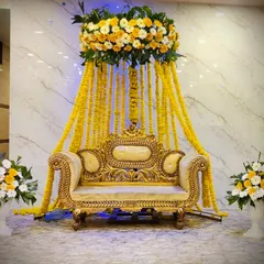 A simple and elegant Haldi setup with a canopy of marigold garlands over a traditional golden sofa.