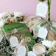 A close-up of the sustainable hamper, highlighting the book "The New York Times Explorer" and other curated items with personalized tags. Each element is chosen to inspire and delight.