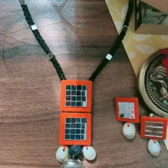 This bold orange necklace and earring set is designed for garba nights. It features large square mirror panels, kowri shells, and a traditional silver-toned pendant for an authentic festive feel.