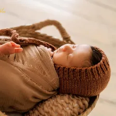 This portrait highlights a cozy knit bonnet and a matching wrap. The textures of the woven basket and soft fabrics add depth and warmth to the image.