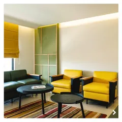 The suite's living area continues the green and yellow color scheme, with contemporary furniture and a vibrant, multi-colored rug. The space is designed to be both stylish and comfortable for guests.