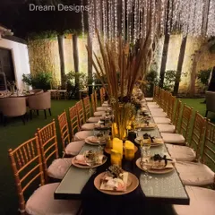 A formal sit-down dinner with a rustic touch. The long table is decorated with tall vases of pampas grass and warm candles, set under a canopy of hanging lights for a magical "dinner under the stars" feel.
