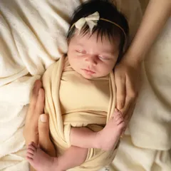 Safely swaddled and sleeping soundly. The simple cream wrap and matching headband keep this portrait feeling natural and pure, with all the focus on the baby's serene face.