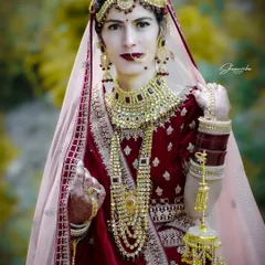 A classic bridal portrait focusing on the rich colors of the velvet lehenga and the intricate gold jewelry. The bride's pose is full of grace and elegance.