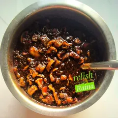 Here is the sweet raw mango pickle being mixed in a large bowl. You can see the chunks of Rajapuri kairi coated in a dark, sweet, and spicy syrup made from sugar and traditional spices like fennel and onion seeds.