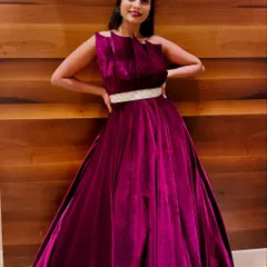 A full-length shot of the magenta velvet gown against a modern wooden backdrop. The pleated bodice and silver belt add a touch of contemporary design to this classic silhouette.