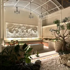 A wider view of the courtyard at night, showing how the lighting design highlights the intricate stone mural, the plants, and the seating area.