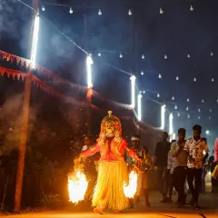 A powerful shot of a Bhoota Kola performer with two large torches, the flames illuminating the smoke-filled path. My low-light photography skills are essential for capturing the raw, spiritual energy of these sacred events.