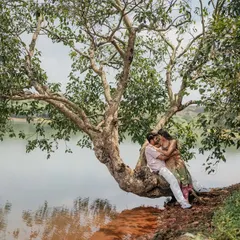 Finding a quiet moment together under a sprawling tree by the water. This wide shot shows the beautiful, peaceful setting for their love story.