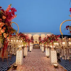 The grand aisle, lined with floral arrangements on pedestals and ornate lanterns. The checkered floor adds a classic touch to the otherwise traditional Rajasthani decor.