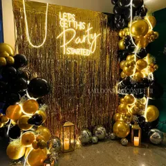 Let's get this party started! A classic black and gold theme gets a modern twist with a gold fringe backdrop, a bold neon sign, and organic balloon arrangements.