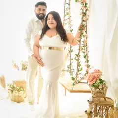 A lovely couple's portrait in matching white outfits. The mom-to-be stands by our floral swing in a beautiful white gown, creating a bright and angelic scene.