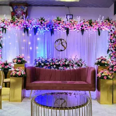 This elegant reception stage features a soft, romantic aesthetic. A floral arch of pink and white roses sits above a backdrop of white curtains and subtle lighting, with a custom monogram adding a personal touch for the couple.