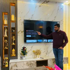 Here I am, pointing to our YouTube channel on a newly installed TV unit at ATS Nobility. The unit features a marble-finish back panel and vertical display niches with gold accents.