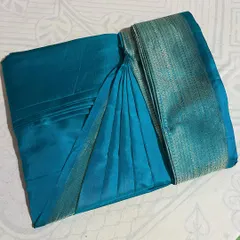 A vibrant teal blue silk saree with a silver border, folded with precision to keep it ready for any event.