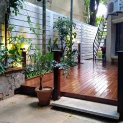 This beautiful villa landscape features a polished wooden deck that serves as a patio. The deck is surrounded by greenery and soft lighting, creating a warm and inviting entrance to the home.