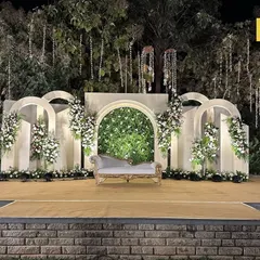 Modern, elegant, and one with nature. This outdoor stage uses clean white arches, a lush green backdrop, and hanging floral installations to create a sophisticated and serene atmosphere for a contemporary wedding.