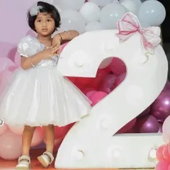Another angle of the white one-shoulder birthday dress, showing its classic A-line shape and fluffy skirt. The design is paired with a delicate hair accessory for a complete and polished party look.
