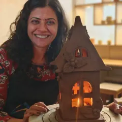 A student proudly smiles with her finished terracotta house lantern, glowing warmly from within. This piece was created using slab-building and decorative sculpting techniques.