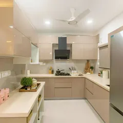 A contemporary U-shaped kitchen in a warm beige tone. The glossy, flat-panel cabinets and white countertops provide a clean, uncluttered look, while the layout maximizes counter space and efficiency.