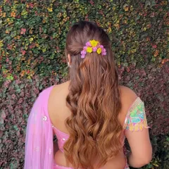 A beautiful half-updo with a simple twist, adorned with a sprig of colorful fresh flowers. This is a perfect hairstyle for a vibrant Mehendi or Haldi ceremony.