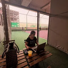 Productivity meets play. A parent works on her laptop in the Parents' Pavilion, with a clear view of the sports action through the net. I make it easy to balance your schedule while your kids are training.