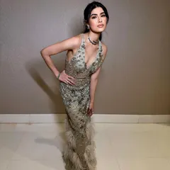 A full-length shot of a glamorous evening look. The makeup is soft and glowing, with a focus on flawless skin, complementing the sequined gown with a feather-trimmed hem.