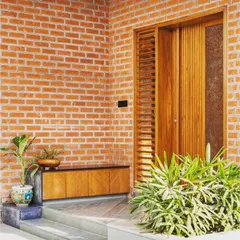 A warm and rustic entrance concept featuring an exposed brick wall. The natural texture of the brick pairs beautifully with the wooden door and simple, low-profile console table, creating an inviting and earthy entryway.