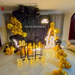 A stylish black and gold theme for an 18th birthday celebration. This setup features a black sequin wall, a "Happy Birthday" neon sign, large marquee numbers, and a dramatic balloon arch, perfect for creating a glamorous party atmosphere.
