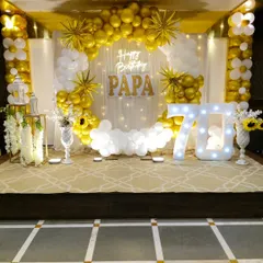 We create elegant setups for milestone celebrations, like this 70th birthday party. The decor features a classic gold and white balloon arch, a sheer curtain backdrop with fairy lights, a custom neon sign, and a large "70" marquee number, creating a sophisticated and celebratory atmosphere.