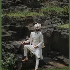 A powerful portrait of the groom in his ivory sherwani, posing against a natural rock formation. The composition is strong and regal, befitting a groom on his wedding day.