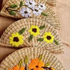 A close-up of our semi-circular woven clutches, each featuring unique, hand-embroidered floral designs like daisies and sunflowers. These details highlight the skill and artistry that go into every piece.