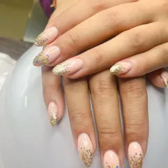 A beautiful example of a glitter fade on long almond nails. This design blends a natural pink base into a sparkling gold glitter tip, making it a popular choice for weddings and celebrations.