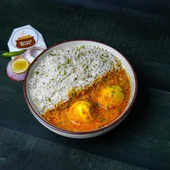 A comforting bowl of egg curry and steamed rice, shot with warm, moody lighting on a dark wooden table.