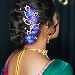 A beautiful and intricate bridal bun decorated with purple flowers and pearl accessories. This hairstyle is both elegant and unique, perfect for a bride who wants something different.