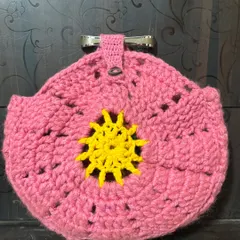 A round, pink crochet potli or pouch with a sunny yellow design in the center, featuring a metal clasp for secure closure.