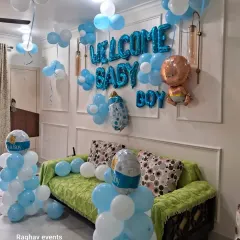 A full living room decoration to welcome a baby boy. The setup includes "WELCOME BABY BOY" foil balloons on the wall, balloon pillars, and loose balloons on the ceiling.